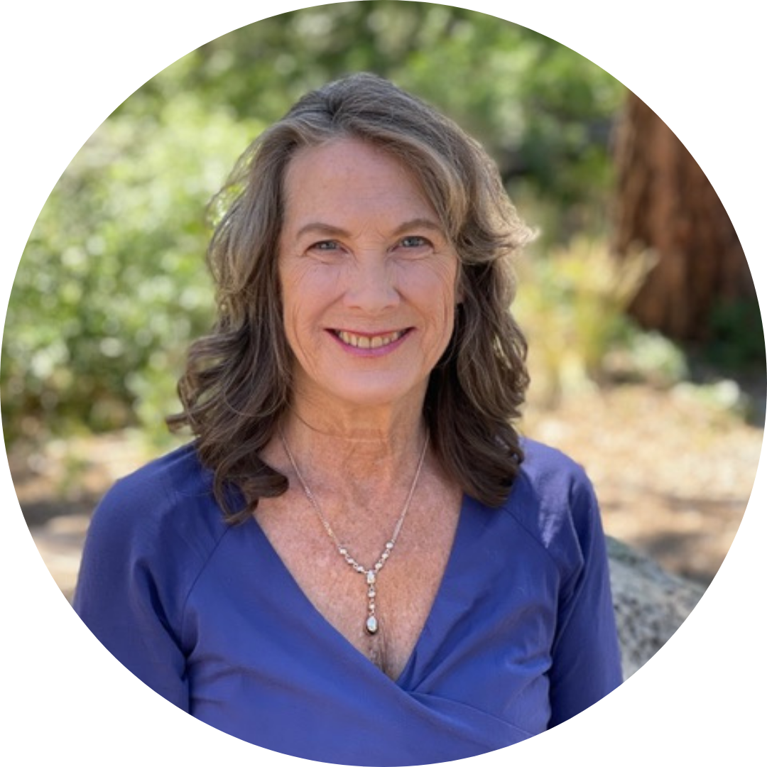 portrait of a smiling woman with shoulder-length wavy hair wearing a blue top and necklace, photographed outdoors